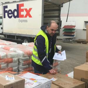 a person checks rows of boxes and wrapped pallets. A fedex truck behind the.