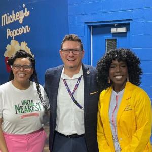Three people posing together and smiling in front of a blue wall