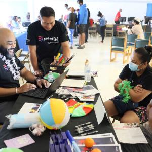 Volunteers with an open laptop talking to two seated people across from them.