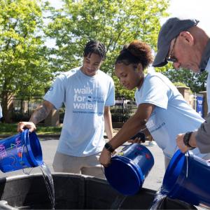 Pouring collected water from individual buckets into one big bucket