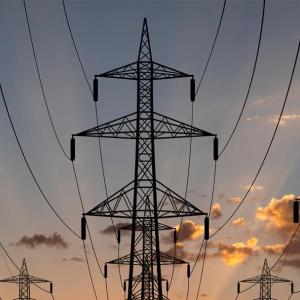 Tall electrical line towers, a setting sun behind them.