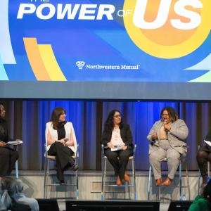 Five people with microphones seated on a stage in front of an audience.