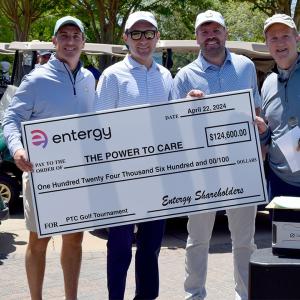 Four people posed with a large check. Golf carts to the side.