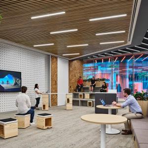 An open space with boxes for seating as well as cushioned benches and circular tables. A person near the front speaking at a podium with display behind them. Windows surrounding. 
