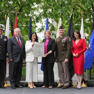 Comcast team members and members of the armed forces holding a document onstage at an event.