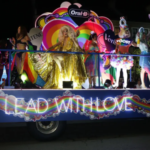 People riding on a pride float with glowing lights that read "Lead with love"