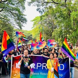 People marching in a parade waving rainbow flags and "Kohler Proud" banner.