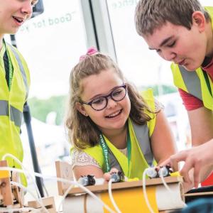 three children in high visibility vests work on an engineering project in a classroom