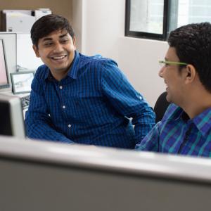 Two men speaking while seated in a cubicle.
