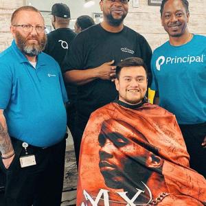 Jonas Cutler seated in a barber chair with three men standing behind him.