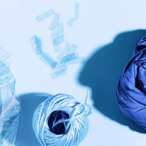 An empty water bottle, spool of thread and piece of fabric all in shades of blue.