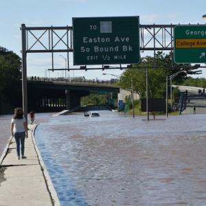 Flooded motorway. Two pedestrians on walkway with street flooded on either side.