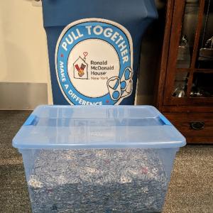 A blue barrel with a label "Pull Together" behind a clear tub full of soda can pull tabs.