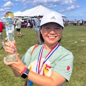 A smiling person holding an award outside.