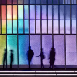 Silhouettes of people behind rainbow colored glass.