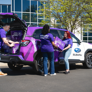 Three people putting boxes into a purple Subaru vehicle