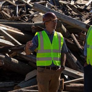 2 workers standing in front of a pile of old power poles