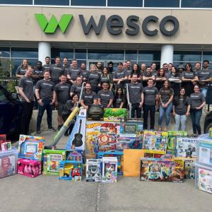 A group standing behind new toys, in front of a Wesco building