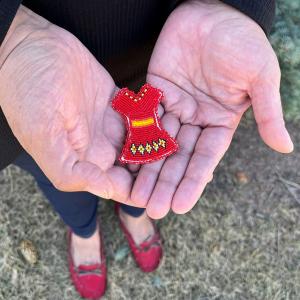 Hands holding a miniature red dress made of beads