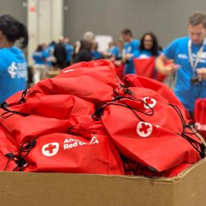 A box filled with American Red Cross bags. Volunteers in the background.