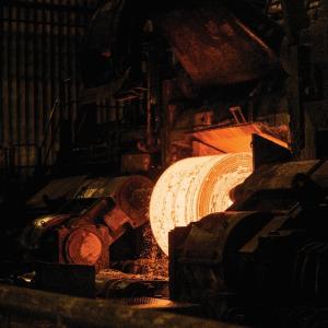 Large steel coil being formed just out of the furnace glows in a dark foundry