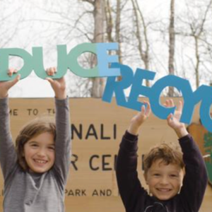 Two children stand in front of a Denali park sign holding up words "Reduce" and "Recycle"