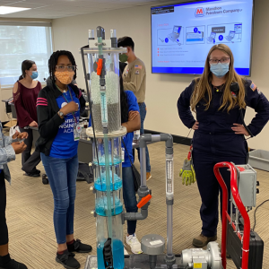 a group of people standing around a model of a distillation tower