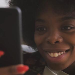 A smiling person looking at a cell phone they're holding in front of them.