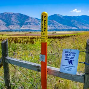 A pipeline marker next to a fence. "Wildlife Refuge" sign next to it.
