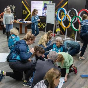 Small groups of people writing on papers on the ground, others walking around the room.