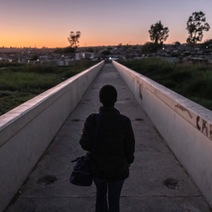A silhouette of a person walking a narrow path towards houses in twilight.