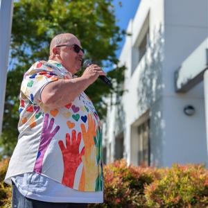 Rene Spring in a colorful handprint shirt speaking outside with a microphone.