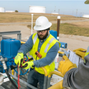 two workers in safety gear, hard hats, gloves work on industrial equipment outside
