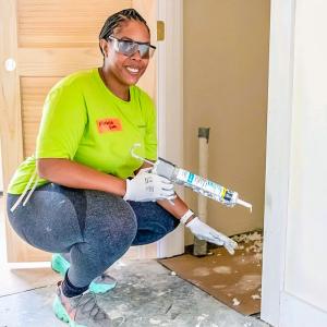 A smiling volunteers holding a caulk gun.