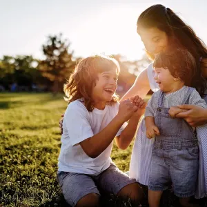 An adult and two children laughing, in an outdoor setting.