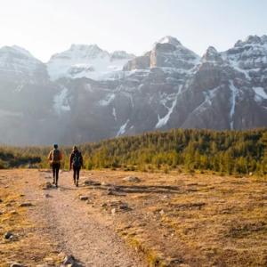 Two people walking away on a dirt path in a mountainous, scenic area.