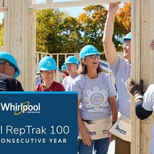 A group of people in matching blue hard hats, some holding wood framing on a construction site.