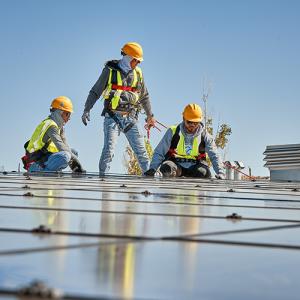 Three people in high-vis garments and hard hats installing solar panels.