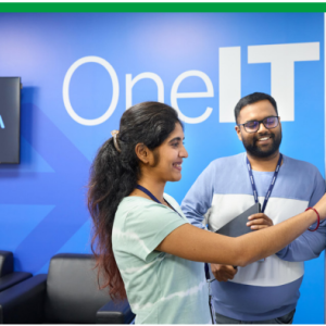 Two smiling people looking at a large touch-screen display. "OneIT" on the wall behind them.