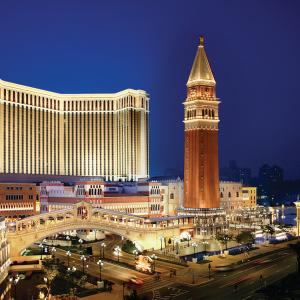 Aerial view of the exterior of a large tower in front of a resort at night.