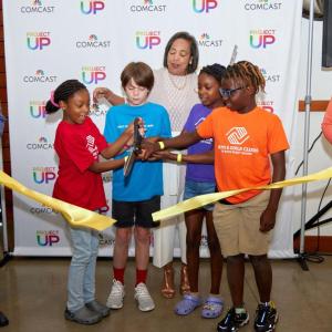Broderick D. Johnson holding a yellow ribbon that a group of children are cutting.