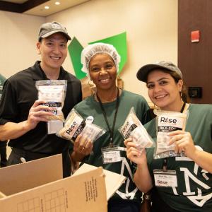 Three smiling volunteers posed, holding "RISE" packs.