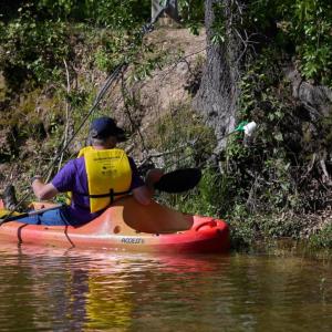 A volunteer in a kayak picking a piece of trash off the river bank.
