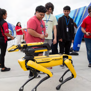Kids and adults watching a robotic dog outside.