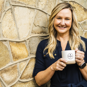 A person holding up a coffee mug next to a tan stone wall.