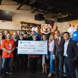 A group posed in a restaurant with a large check. A tiger mascot behind them.
