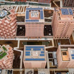 Aerial view of rows of tall buildings, most with solar panels on the roofs.