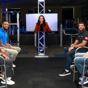 a group of four people an a person appearing on a monitor all seated in a studio