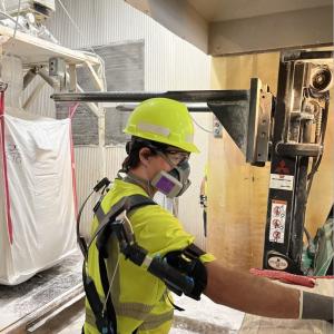 A person in protective gear in a manufacturing area wearing an 'exoskeleton' on their back.