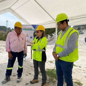 Three people talking under a canopy, each wearing hard hats and high-vis clothing.